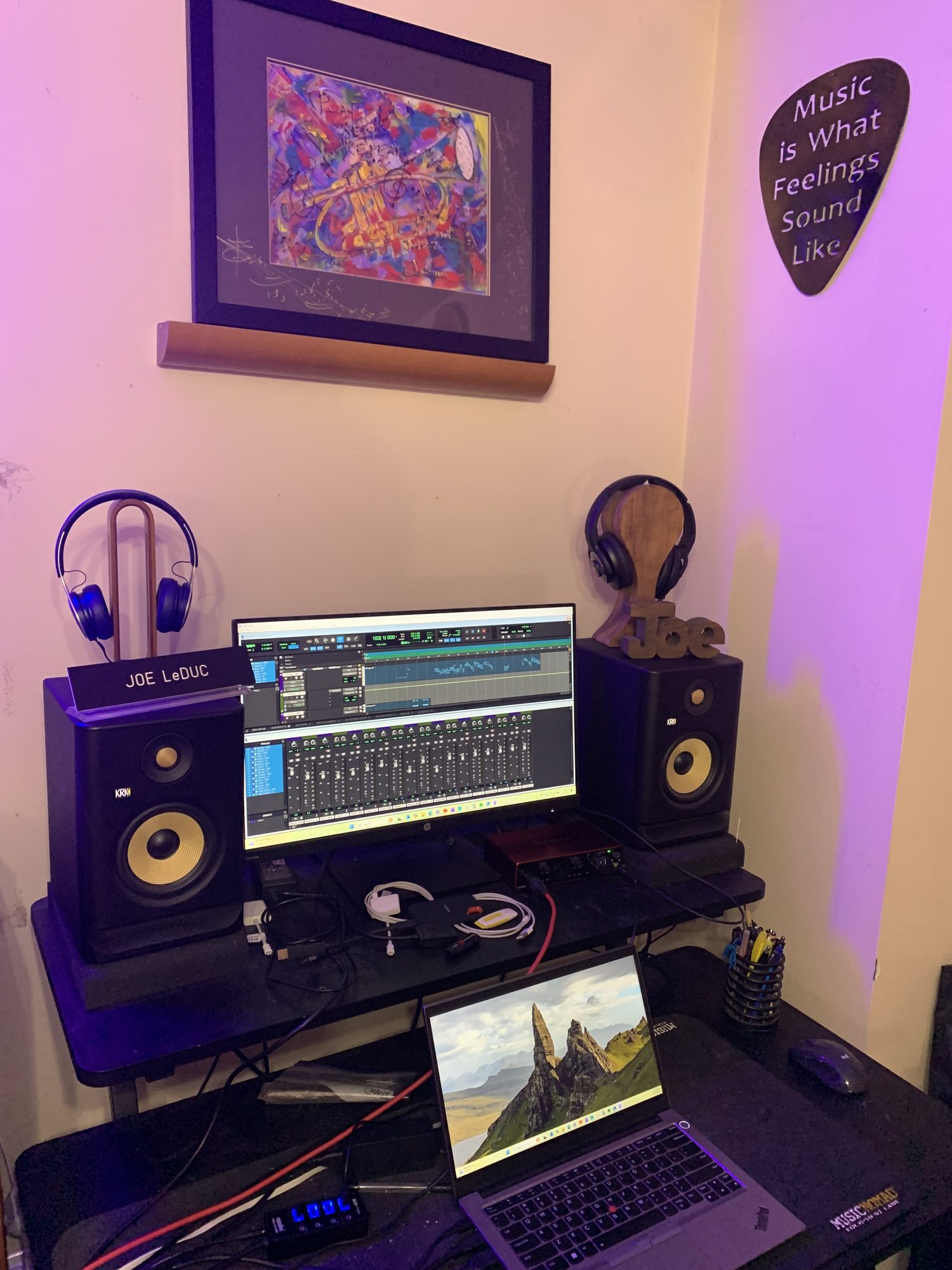Blue-lit control room desk with studio monitors, headphones, and a laptop running Pro Tools